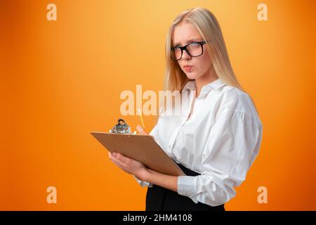 Teen school girl taking notes on clipboard against orange background Stock Photo