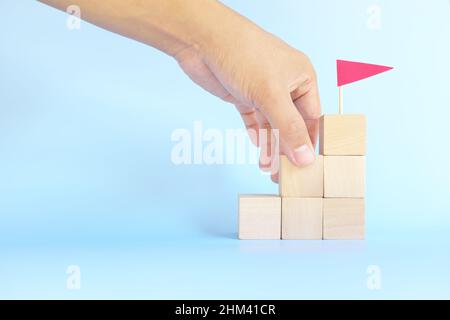 Help and management support in building ladder to success concept. Wooden blocks with red flag on top. Stock Photo