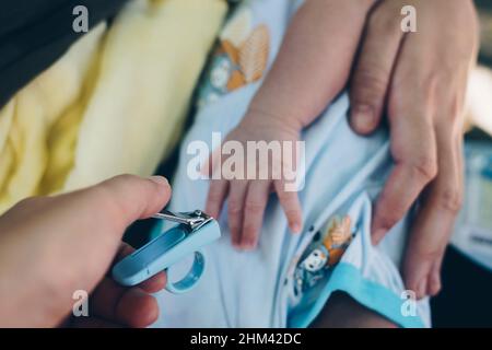 Hand holding a blue clipper to trim the baby's long fingernails for first time. Personal perspective. Stock Photo
