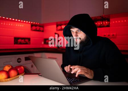 a hacker in a black hoodie is sitting at a laptop hacking the Internet security system Stock Photo