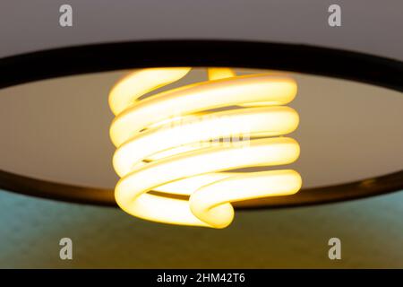 Close-up on glowing energy efficient spiral light bulb sticking from wall lamp Stock Photo