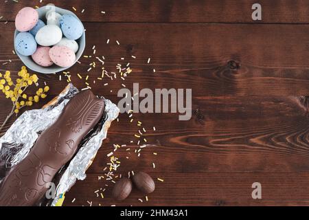 Easter eggs and chocolate bunny on dark wooden background with yellow flower decorations. Top view. Copy space. Stock Photo