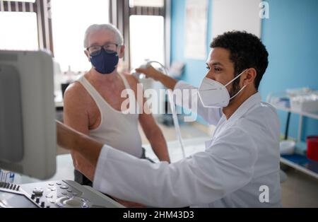 Young doctor is examining senior patient by using an ultrasound equipment in clinic. Stock Photo