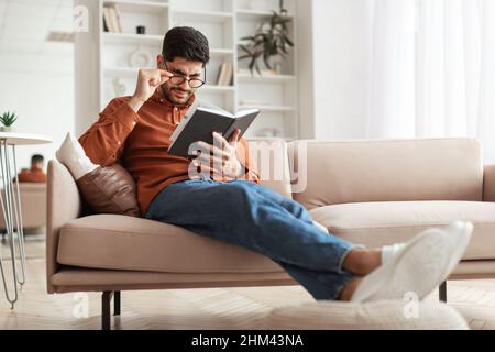 Focused Arab man in glasses trying to read book Stock Photo