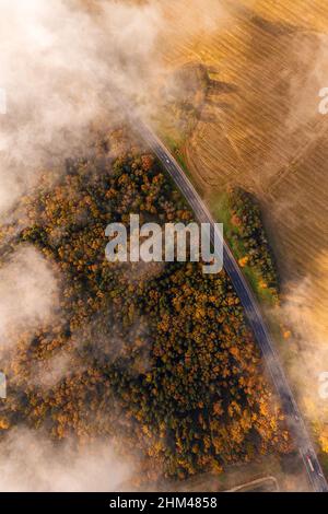 Aerial view on a rural highway during fall season. Autumn bright foliage and cars moving through clouds of fog Stock Photo