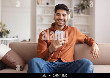 Smiling bearded man in wireless headhones using cellphone Stock Photo