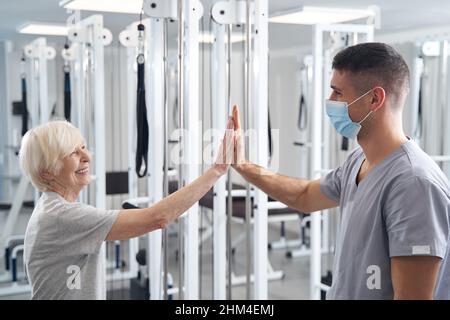 Joyful elderly female giving high five to her doctor Stock Photo
