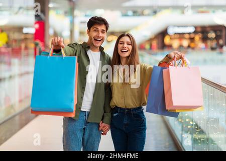 Cheerful Spouses Showing Shopping Bags To Camera Standing In Mall Stock Photo