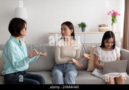Stressed young Asian woman having conflict with her senior mother about daughter's gadget overuse at home Stock Photo