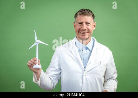 Scientist with white coat holds miniature wind turbine against green background Stock Photo