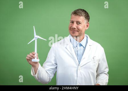 Scientist with white coat holds miniature wind turbine against green background Stock Photo