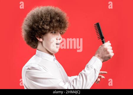 A curly-haired man in a shirt holds a comb in his hands, looks at him. Salon. Comb curly hair. Stock Photo