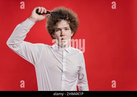 Comb curly hair. A curly-haired man in a shirt is brushing his curly one. Beauty saloon Stock Photo