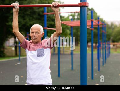 Elderly man hanging from pullup bar and doing pull-ups Stock Photo
