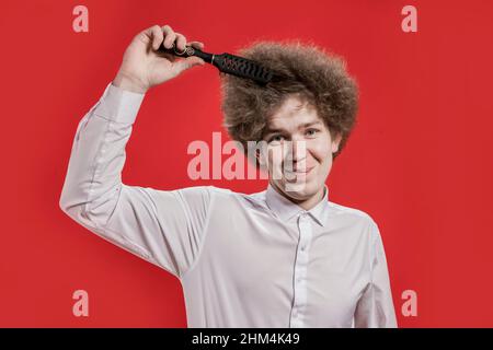 A curly-haired man in a shirt smiles and brushes his curly hair. Comb curly hair. Salon. Stock Photo