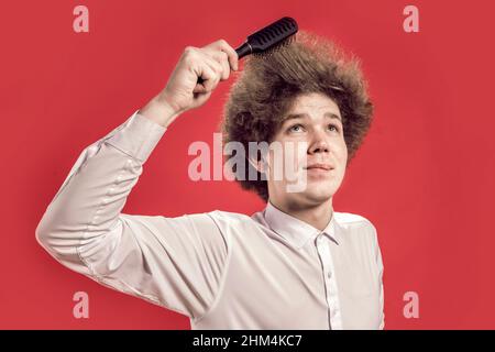 Salon. A curly-haired man in a shirt combing his hair, looking up. Comb curly hair. Stock Photo
