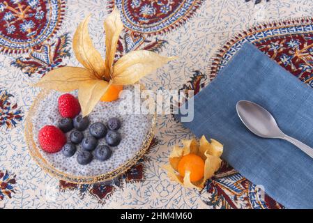 High angle close-up of chia pudding dessert with summer berries, raspberries, blueberries, bananas and physalis. Flat lay, top down view, no people. Stock Photo