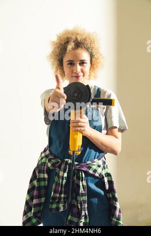 Young crafty gilr showing the thumb up gesture while holding the disc angle grinder. High quality photo Stock Photo