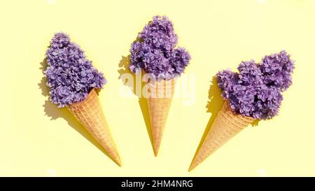 Ice cream waffle cones with lilac flowers on a lemon yellow background. Cool floral ice cream in lavender color for hot summer days concept. Stock Photo