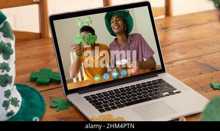 Webcam view of two african american men drinking beers on video call on laptop on wooden table Stock Photo