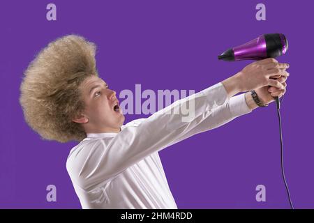 To dry hair. Beautiful hairstyle. Funny student. Shaggy guy. Direct air towards yourself. Loser. Humor. Handsome red-haired man holding a hairdryer in Stock Photo