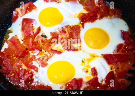 Fried eggs with tomatoes on a frying pan. Close-up, selective focus. Stock Photo