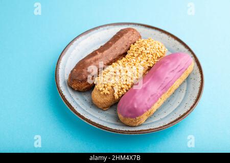 Set of eclair, traditional french dessert on ceramic plate on blue pastel background. side view, close up, still life. Breakfast, morning, concept. Stock Photo
