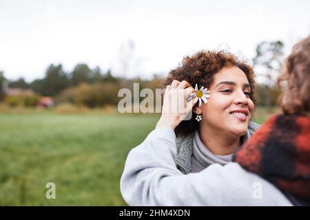 Woman putting flower behind friend's ear Stock Photo