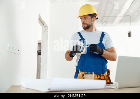 Busy handyman, electrician using insulating tape while installing new electrical socket outlet in apartment Stock Photo