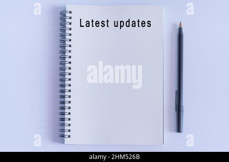 Latest updates text on notepad with pen on white background. News concept. Flat lay with open book page Stock Photo