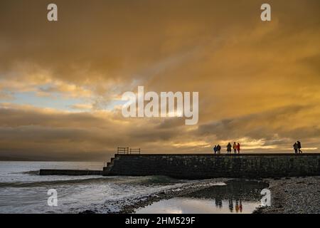 People on the breakwater at Criccieth North Wales at Sunset Stock Photo