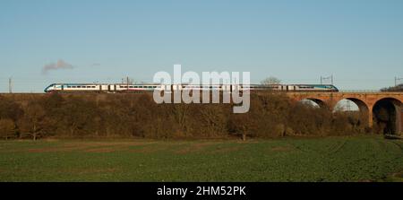 Trans Pennine passenger train passing over viaduct crossing valley and farmland on late autumn afternoon Stock Photo