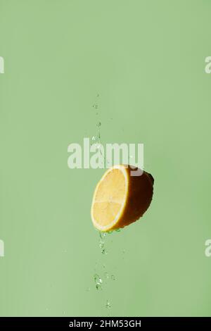 A cut juicy half of a lemon with splashes of water on a green background. Front view. Levitation. Stock Photo