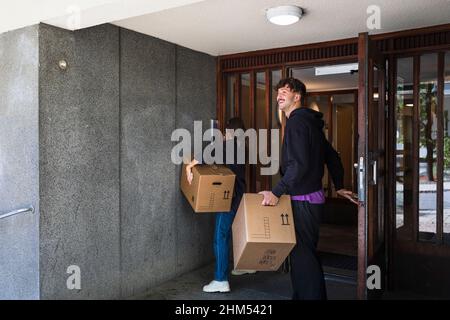 Couple entering building carrying boxes