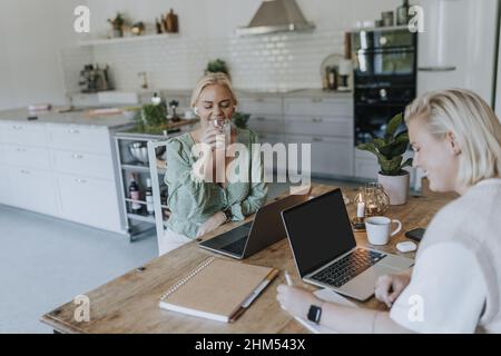 Women using laptops in kitchen Stock Photo