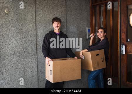 Smiling couple carrying boxes and holding keys Stock Photo