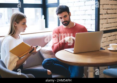 Focused man and woman watching news on laptop in cafe Stock Photo