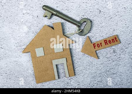 For rent text on brown arrow and paper house model with key on floor tiles. Concept for real estate property, buy or rent. Stock Photo