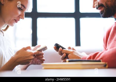 Young smiling friends browsing smartphones together in modern cafe Stock Photo
