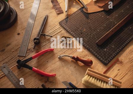 High angle view of various leather tools with cutting mat on wooden table in workshop Stock Photo