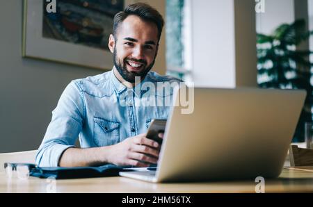 Smiling freelancer using smartphone while working on laptop Stock Photo