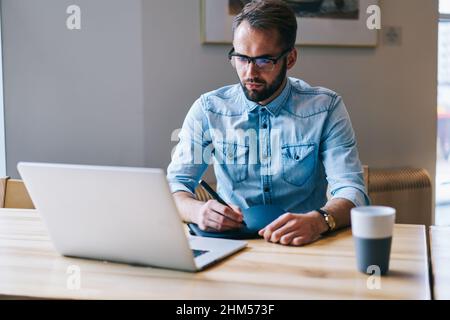 Focused man looking at laptop taking notes Stock Photo