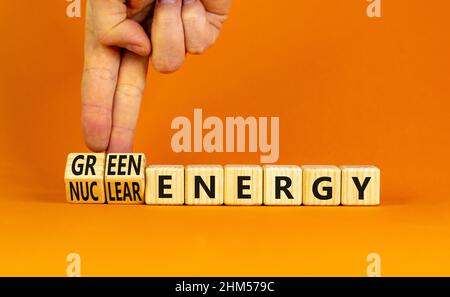 Nuclear or green energy symbol. Businessman turns wooden cubes and changes concept words nuclear energy to green energy. Beautiful orange background c Stock Photo