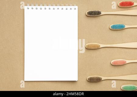 Multiple multicolor bamboo toothbrushes are lying on craft eco paper near notepad. Copy space, top view. Stock Photo