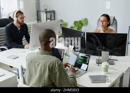 Three young intercultural diversity programmers sitting by desks in front of computers and developing new programs Stock Photo