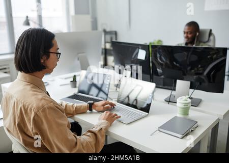 Young Asian male programmer looking at decoded data on laptop screen while working over development of new programs in office Stock Photo