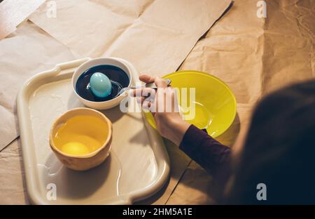Coloring eggs for easter. Put egg with spoon to yellow paint Stock Photo