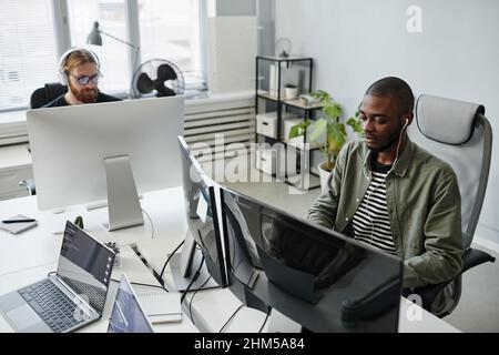 Young serious diversity programmer in casual clothes looking through data on computer screen while working over new project Stock Photo