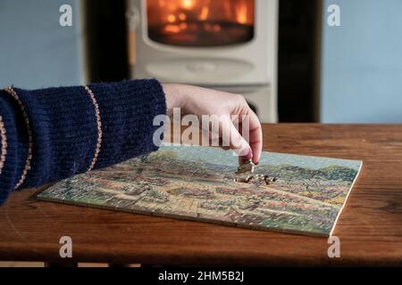 A woman sits next to a wood burning stove as she pieces together a vintage  Victory Artistic 1930s wooden puzzle Stock Photo - Alamy
