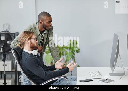 Two young contemporary diversity programmers discussing data on computer screen while one of them making presentation Stock Photo